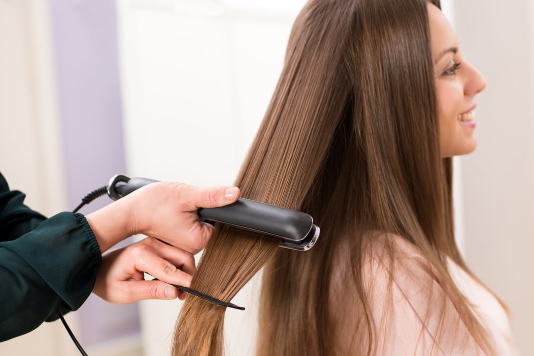 Hairstylist Using a Flat Iron to Straighten Woman's Hair 